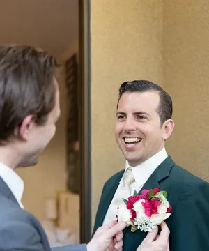 Taylor Hughes smiling as a boutonniere is pinned to his suit
